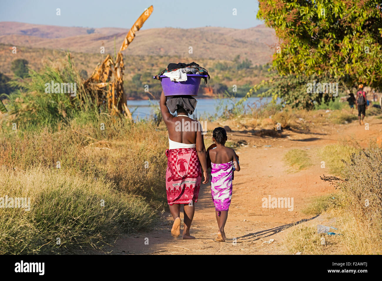Un malgascio la figlia e la madre con un cesto della biancheria sulla testa mentre passeggiate lungo il fiume Tsiribihina, Miandrivazo, Menabe, Madagascar Foto Stock
