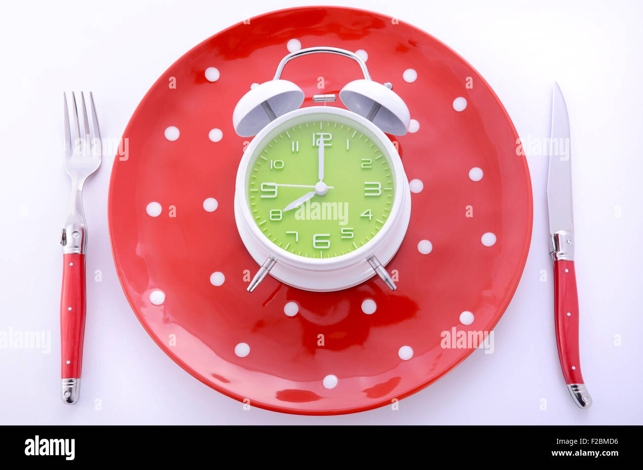 Moderno e luminoso posto tabella di impostazione con la polka dot piatti e posate su sfondo bianco con clock set per otto oclock. Foto Stock