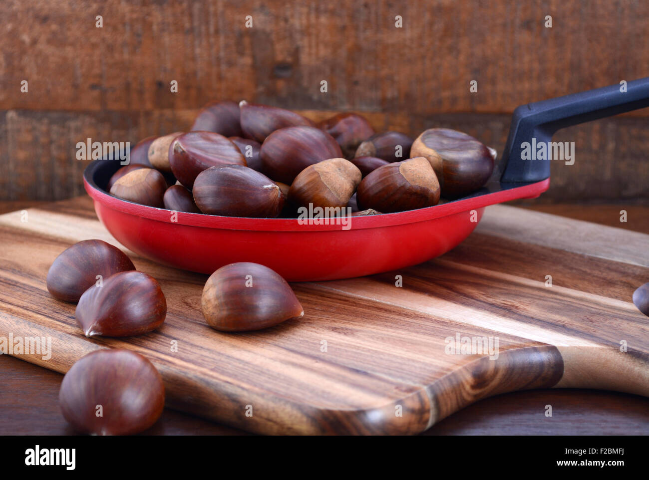 Le castagne in padella frypan sul tagliere di legno contro il legno scuro tavolo rustico. Foto Stock