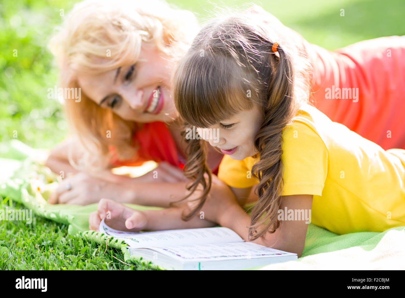 Madre la lettura di un libro per bambini all'aperto in estate Foto Stock