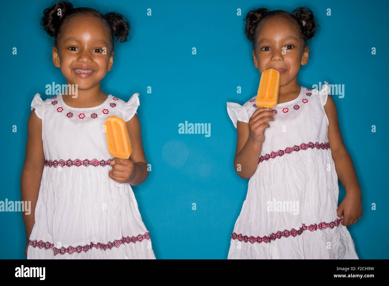 Due identici due gemelle mangiare popscicles su sfondo blu Foto Stock
