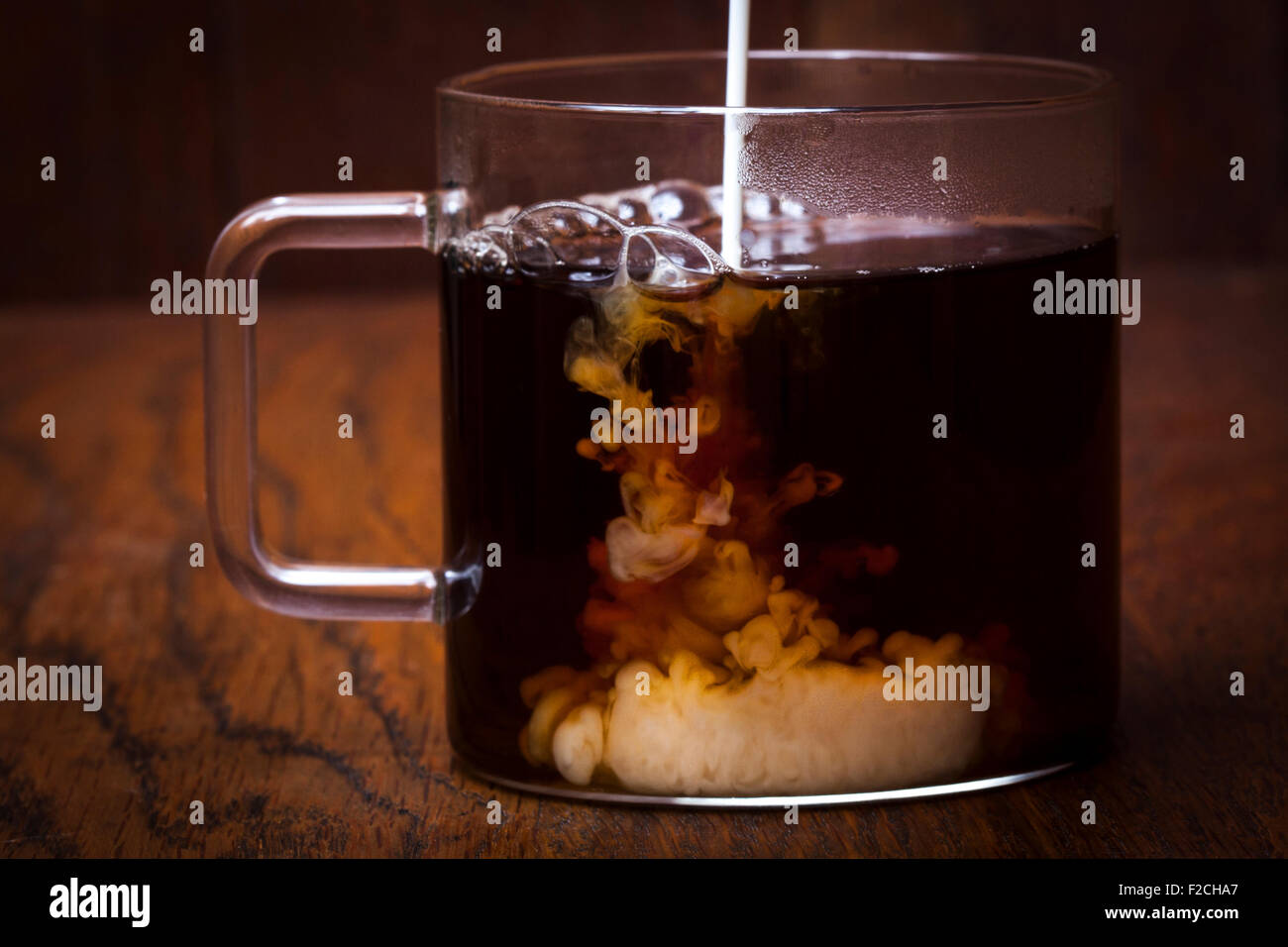 La crema che viene versato in caffè in tazza di vetro Foto Stock