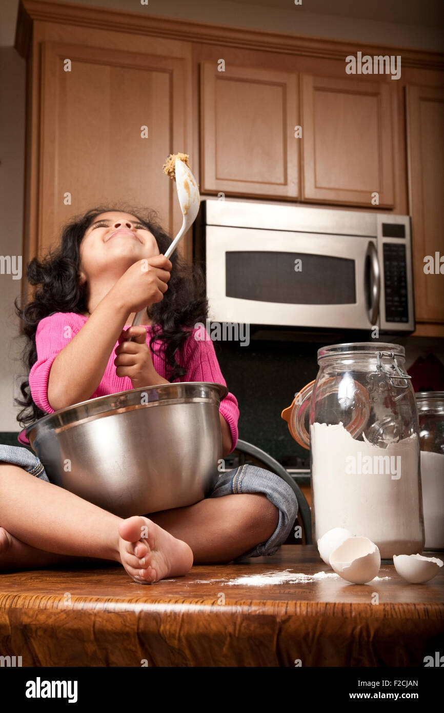 Ragazza giovane con la cima rosa siede sul bancone cucina cibo di miscelazione in acciaio inox con una ciotola Foto Stock