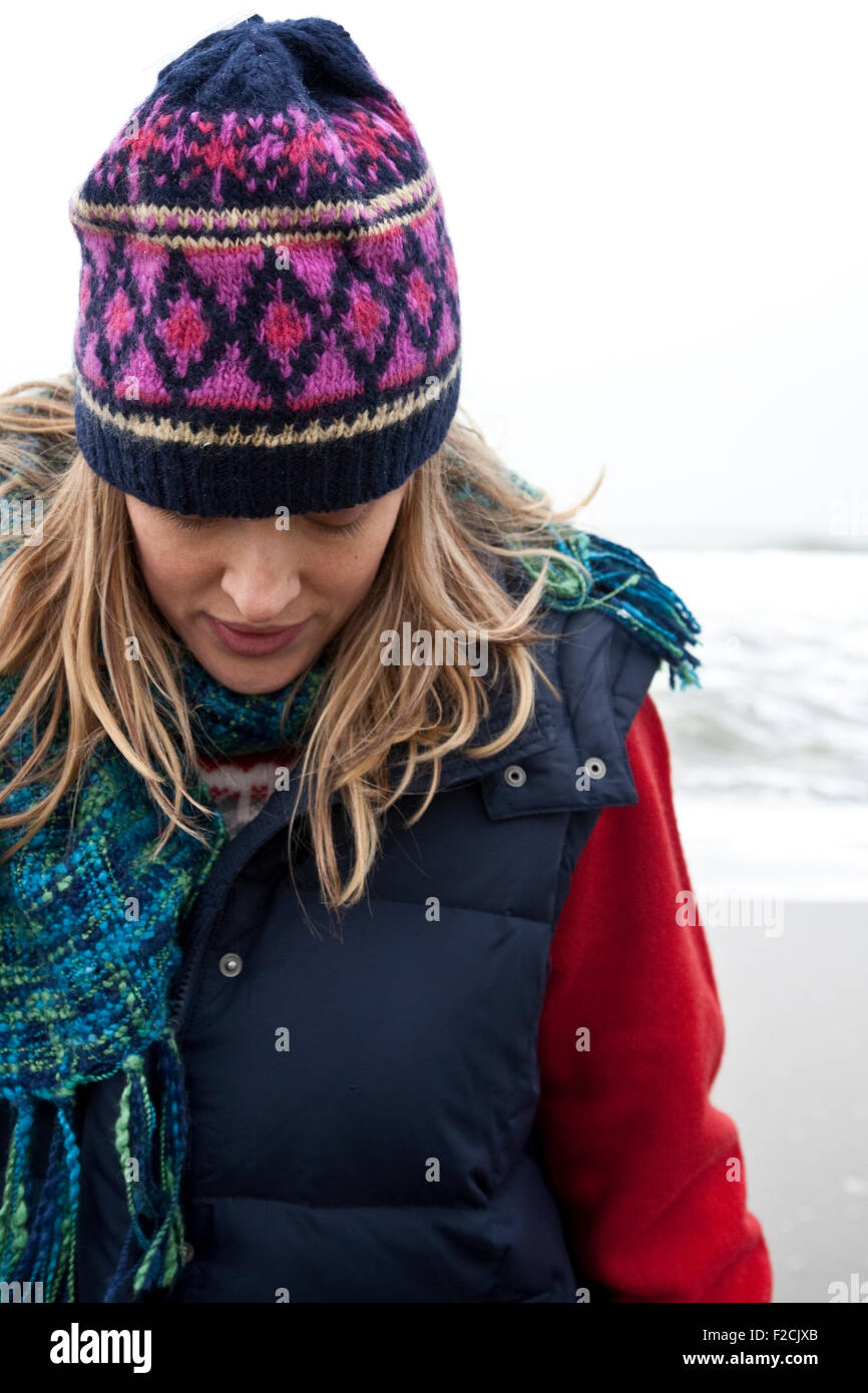 Close-up di giovane donna che guarda verso il basso, indossare abbigliamento invernale in spiaggia Foto Stock