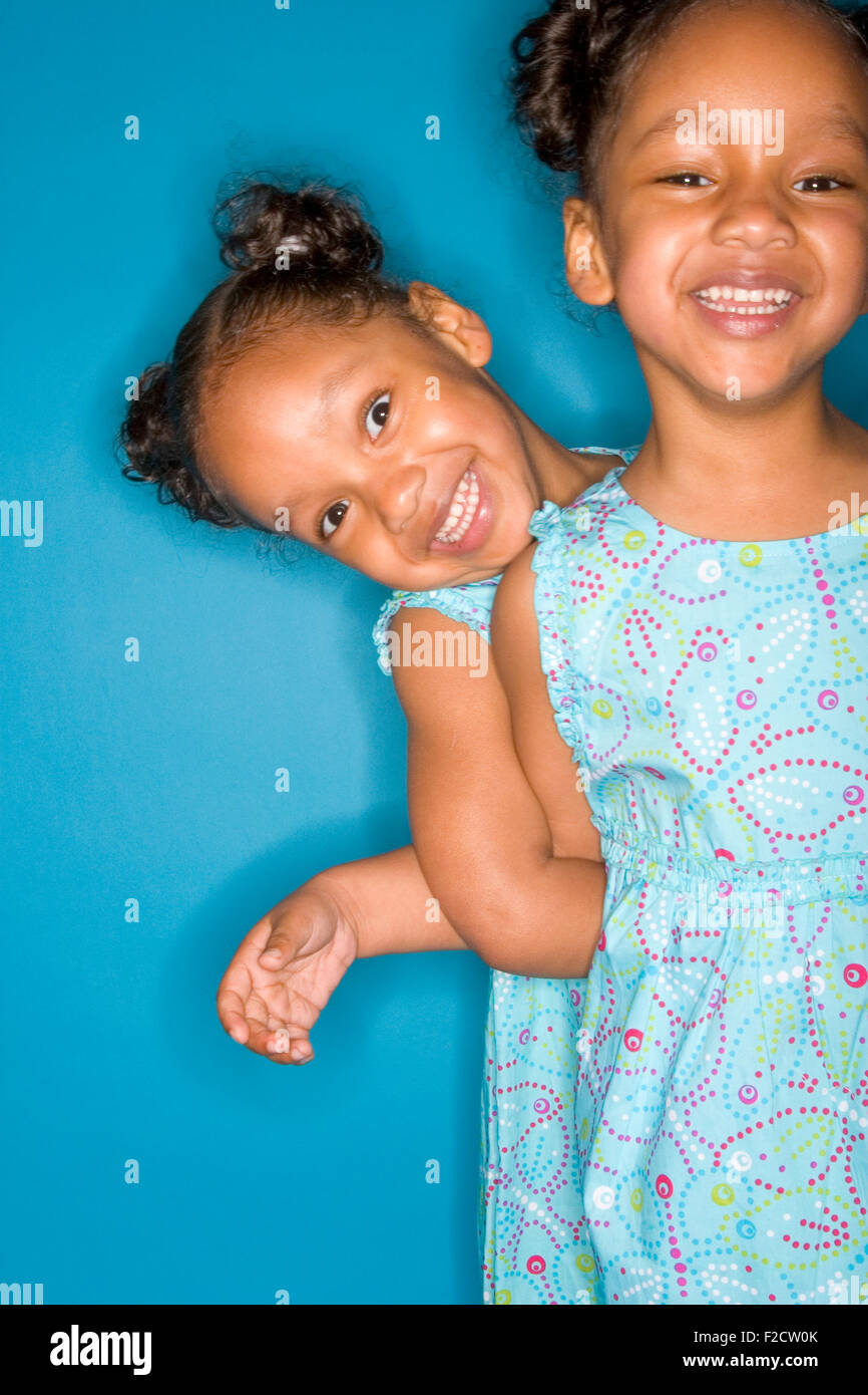 Due ragazze sorridenti gemelli identici indossando sundresses blu, uno dietro l'altro in un blu, impostazione di studio Foto Stock