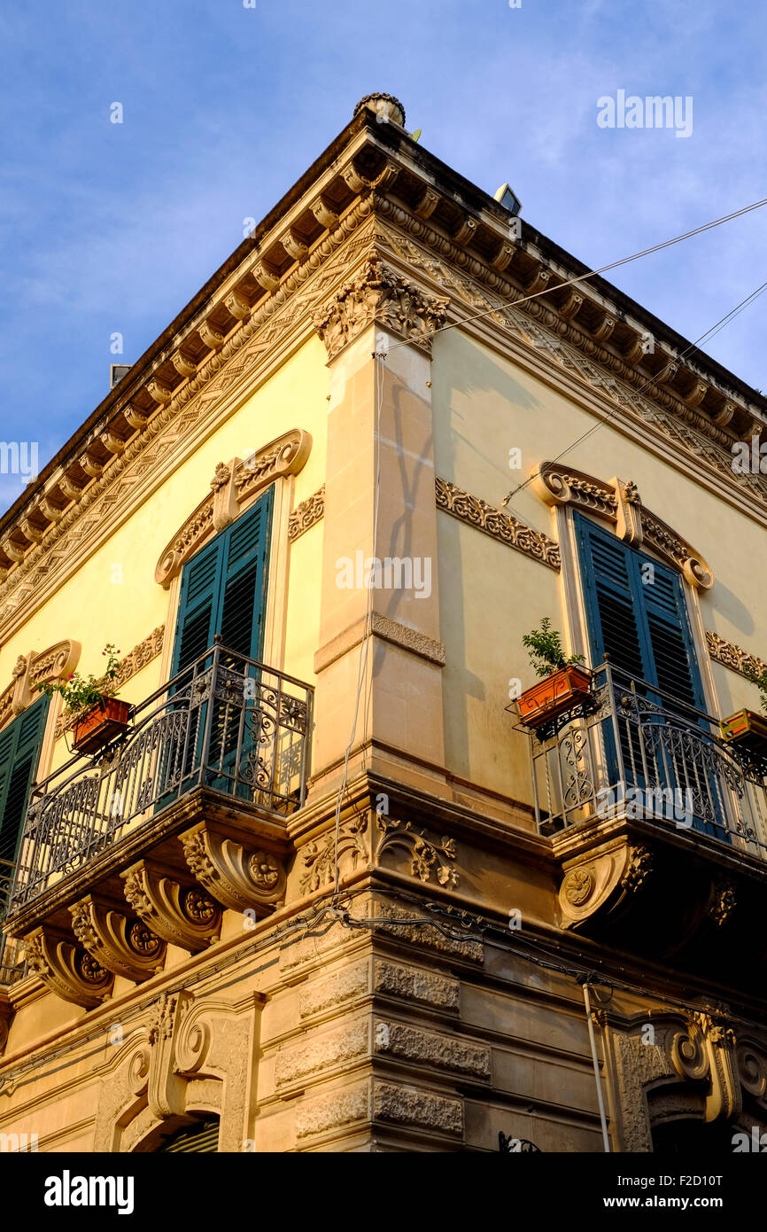 Un basso angolo di vista di intricati balconi in ferro battuto su un angolo di strada nel barocco strada principale di Noto, Sicilia, Italia Foto Stock