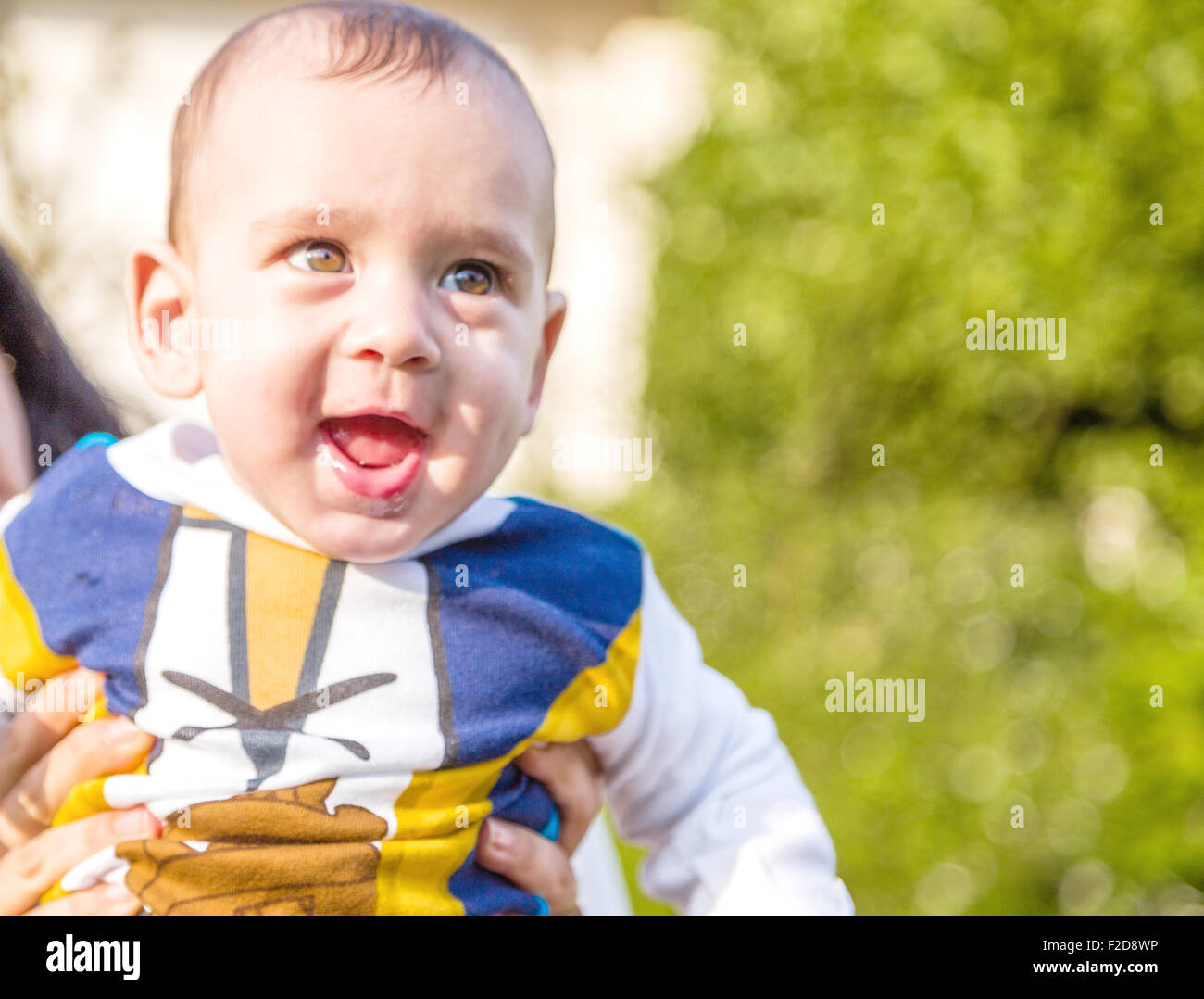 Carino 6 mesi baby con luce marrone capelli in bianco, blu e bruno camicia a maniche lunghe è abbracciato e tenuto da sua madre: egli sembra molto felice Foto Stock
