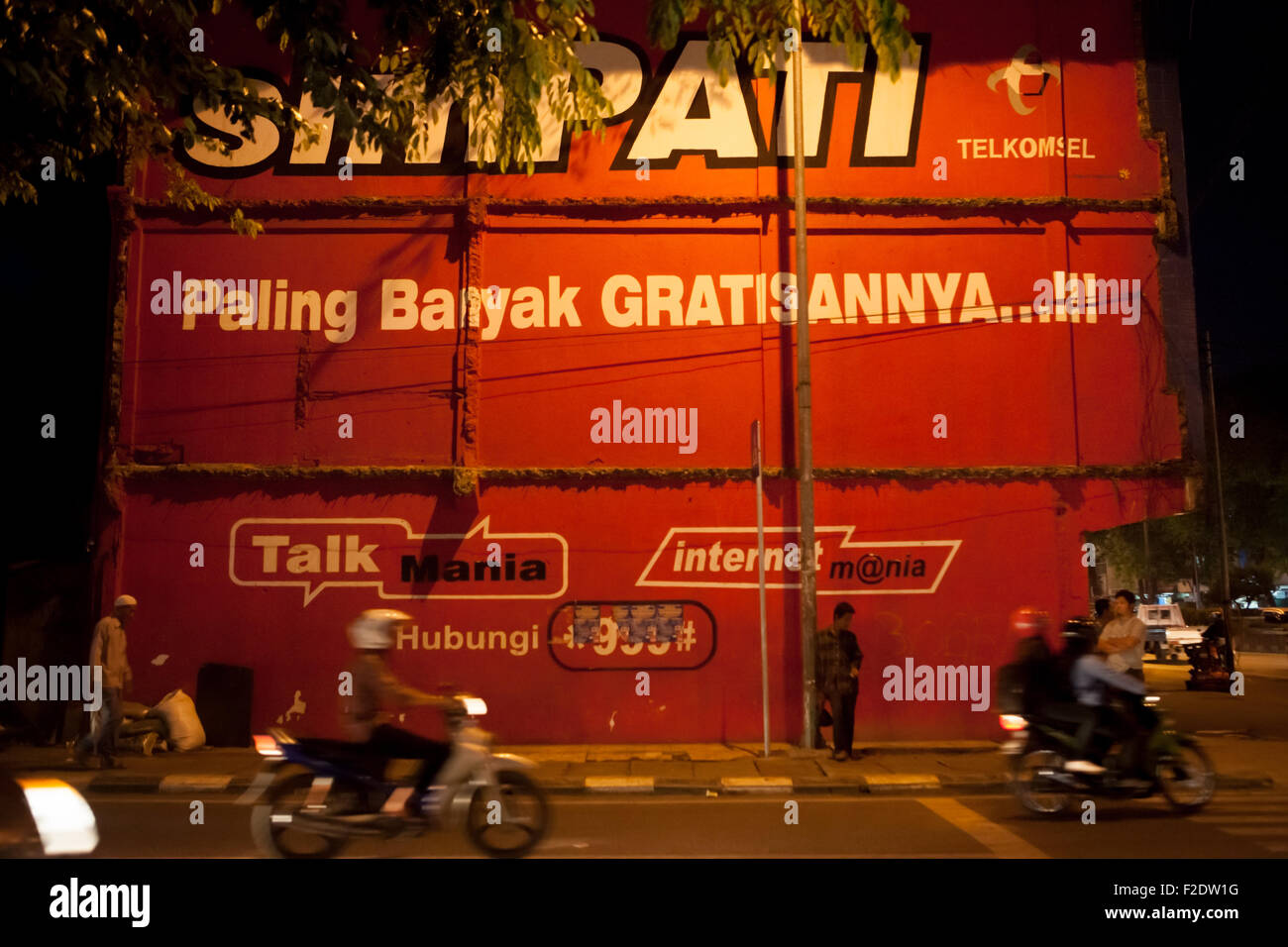 Persone in piedi e camminare su un marciapiede di fronte a un edificio muro decorato con un prodotto pubblicitario a Palembang, Sumatra Sud, Indonesia. Foto Stock