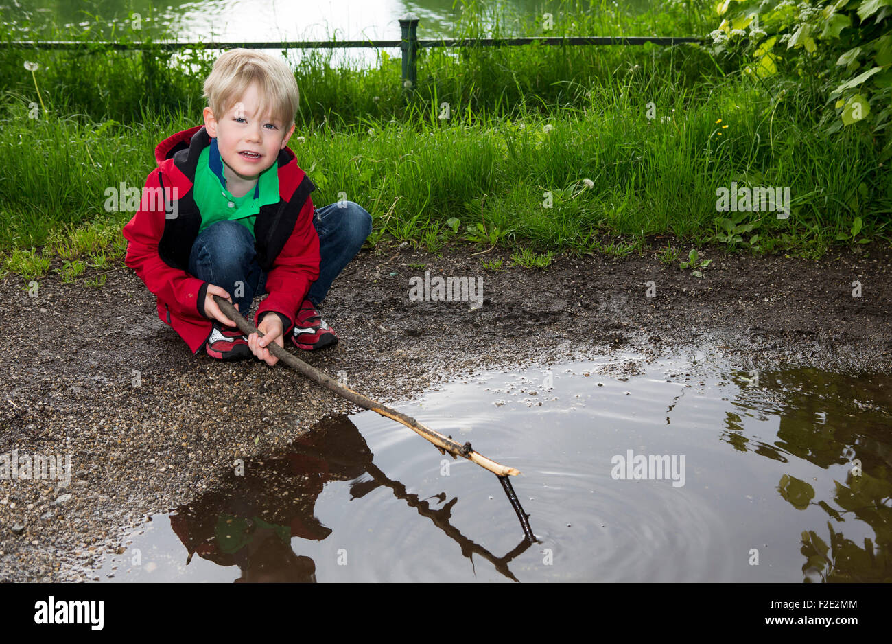 Bionda e giovane ragazzo giocando con il bastone a una pozzanghera Foto Stock