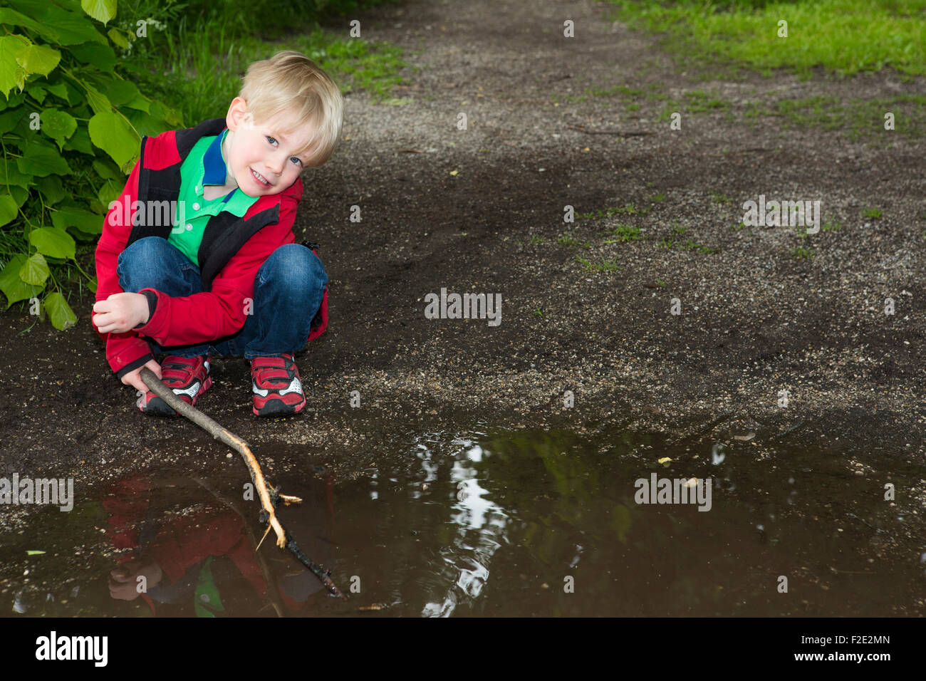 Bionda e giovane ragazzo giocando con il bastone a una pozzanghera Foto Stock