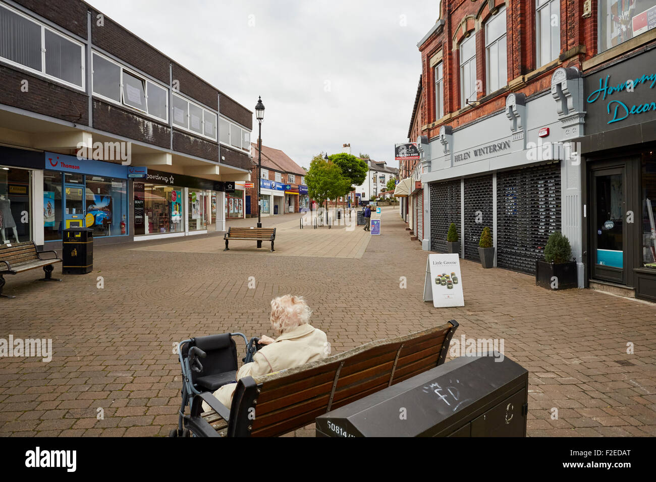 Una vecchia signora siede su un banco a Marple shopping parade Foto Stock