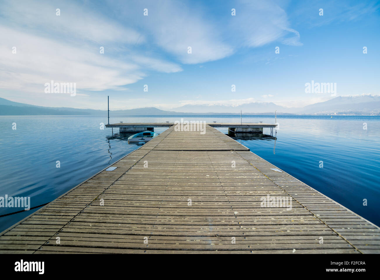 Vista prospettica da un pontile in legno, calma acqua di lago, i trend con orizzonte di riferimento e montagne sullo sfondo Foto Stock