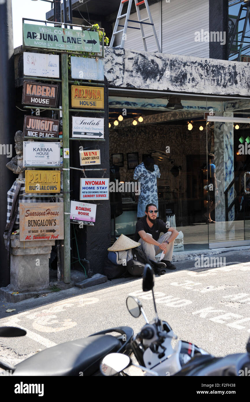 Un turista caucasici seduta segnaletica sotto il nome di hotel in Monkey Forest street, Ubud, Bali Foto Stock