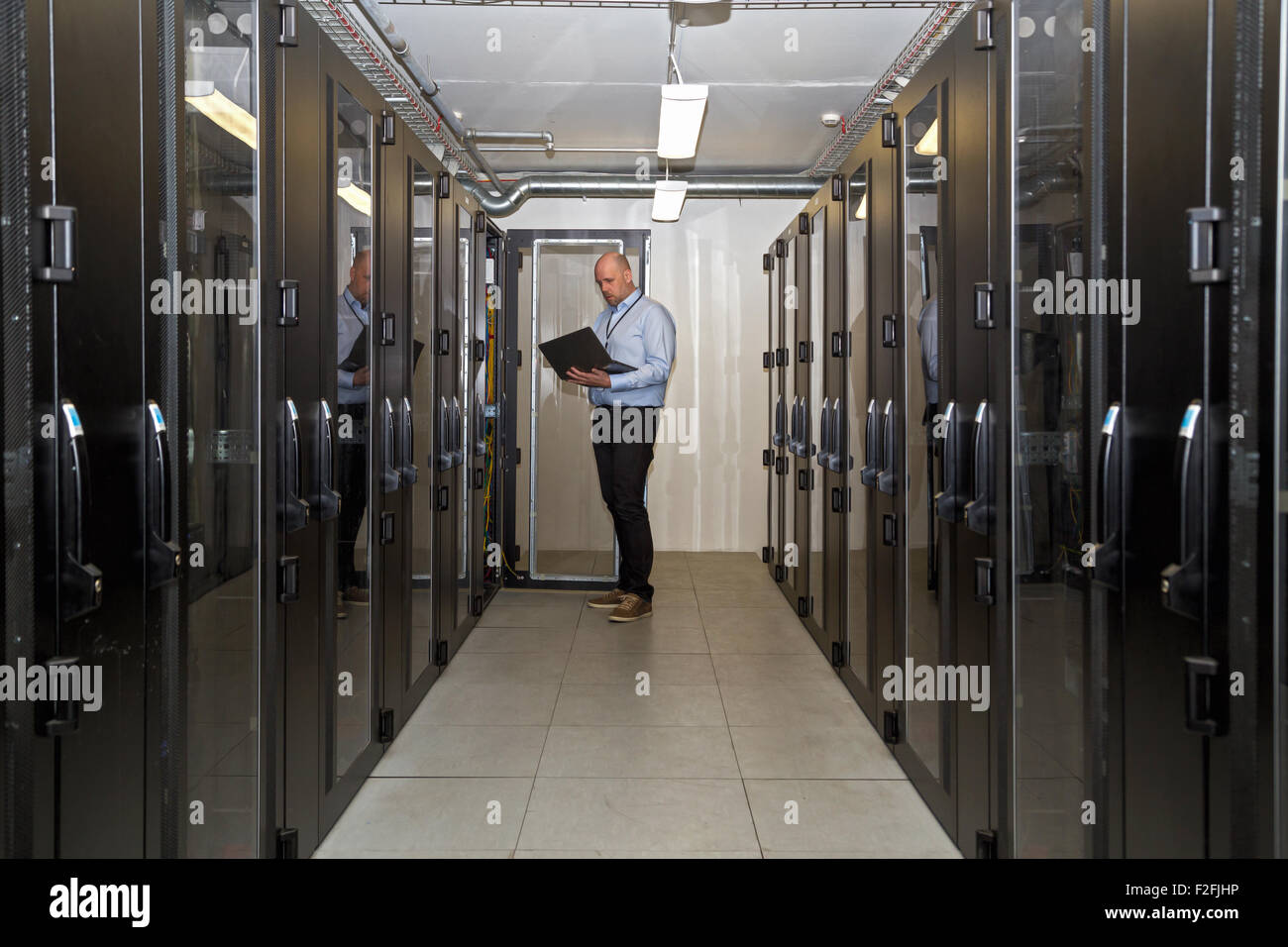 Amministratore server lavora fino a tardi su di aggiornare i server in una sala server al di fuori degli orari di ufficio, in possesso di un computer portatile per verificare su progre Foto Stock