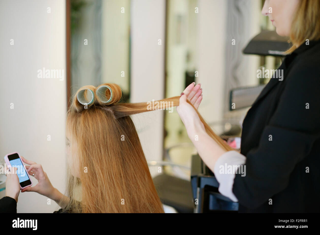 Parrucchiere il rotolamento del cliente in capelli arricciacapelli in salone Foto Stock