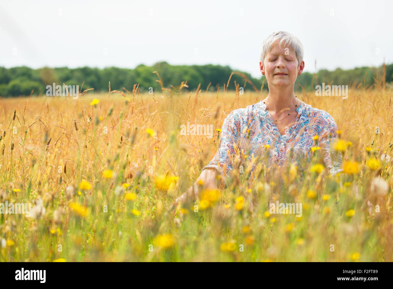 Senior donna meditando in campo rurale Foto Stock