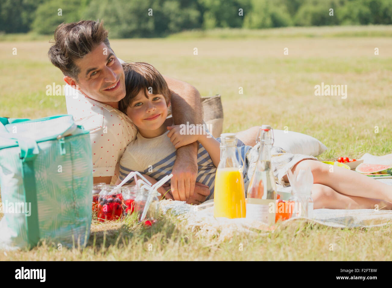 Ritratto affettuoso padre e figlio rilassante sulla coperta picnic in campo soleggiato Foto Stock