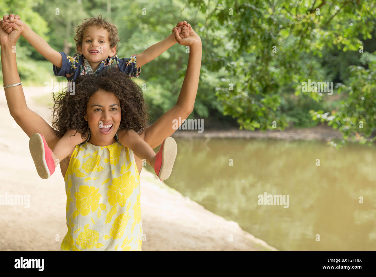 Ritratto giocoso madre figlio che porta sulle spalle nei pressi di stagno Foto Stock
