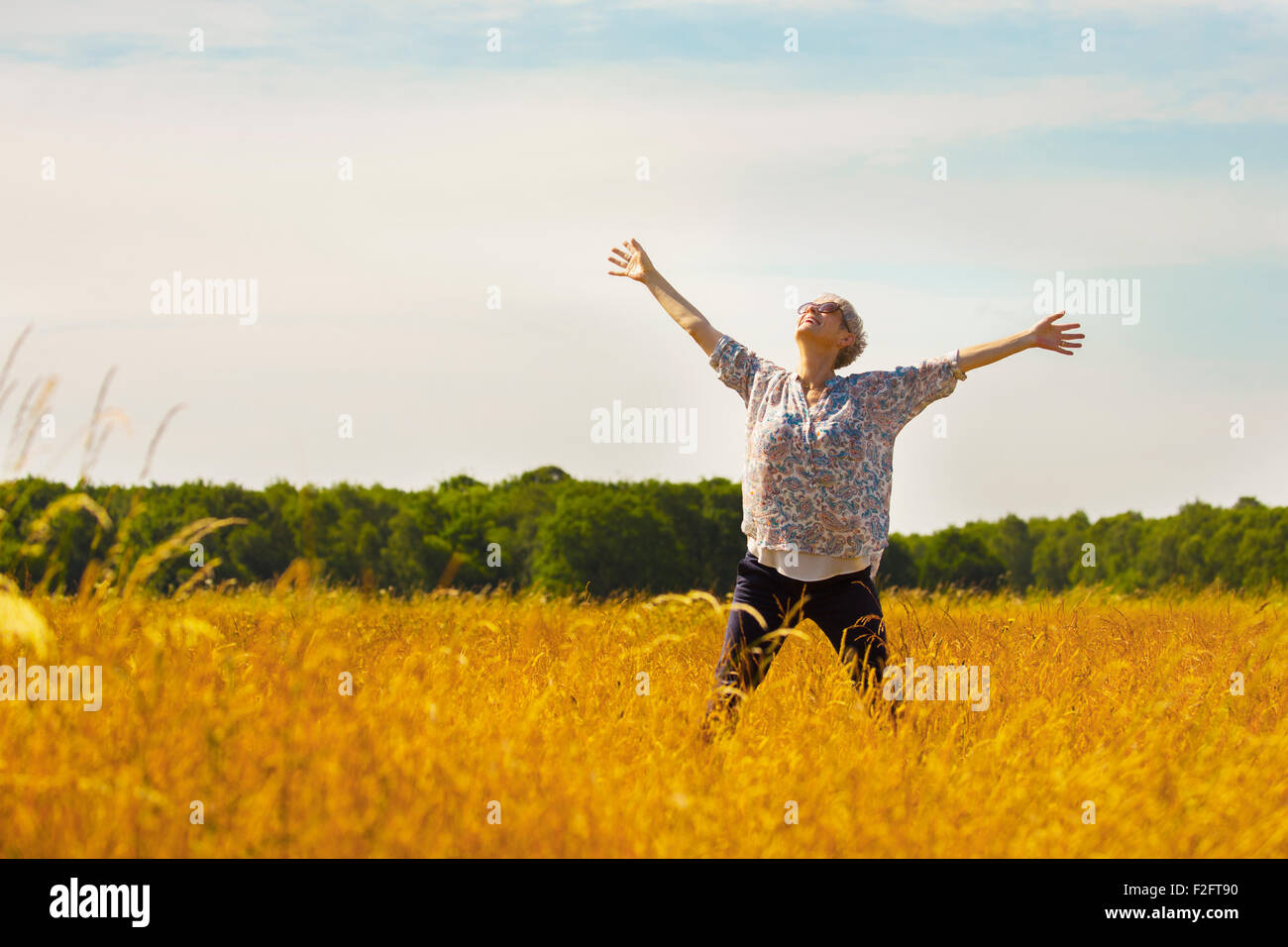 Senior esuberante donna con le braccia aperte nel soleggiato campo rurale Foto Stock