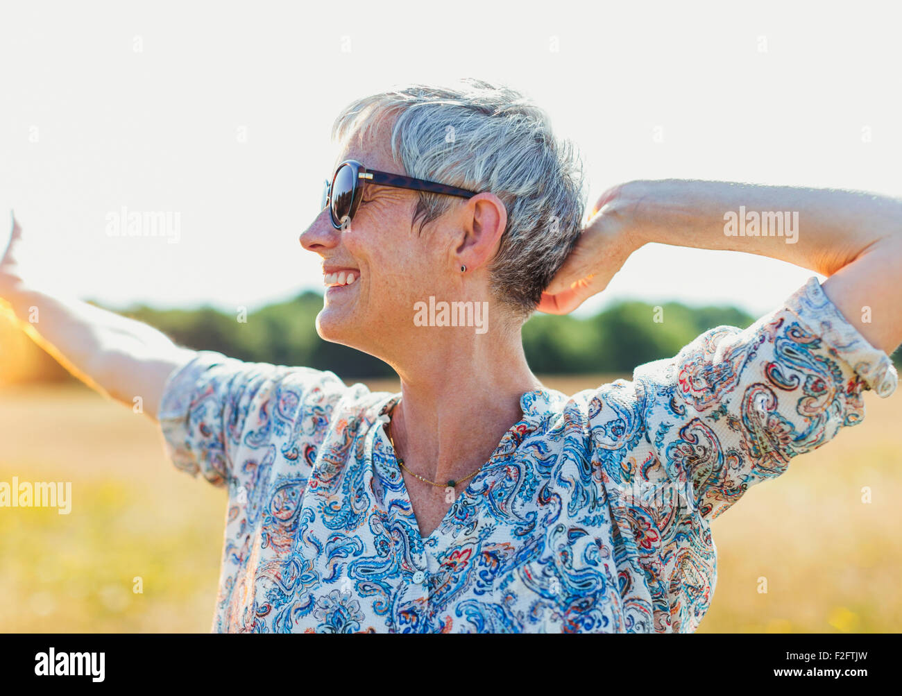 Entusiasta il senior donna con le braccia aperte nel campo soleggiato Foto Stock
