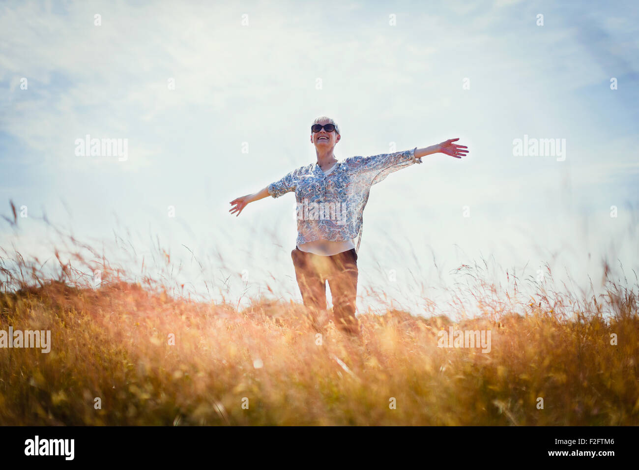 Carefree senior donna in corsa con le braccia aperte nel campo soleggiato Foto Stock