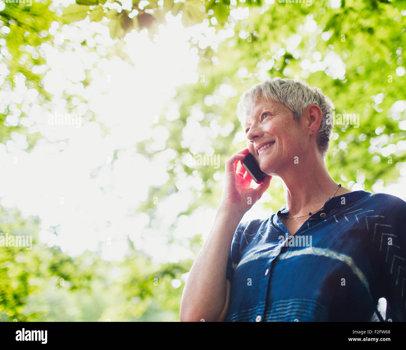 Sorridente donna senior parlando al cellulare al di sotto degli alberi Foto Stock