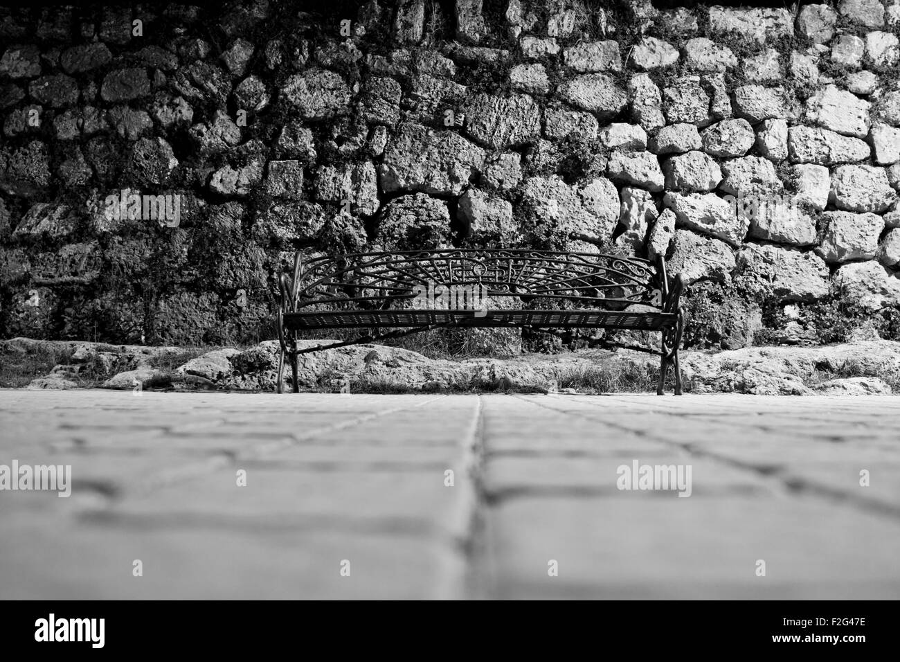 Immagine in bianco e nero di ferro battuto panchina dal livello del suolo con parete lapideo in background Foto Stock