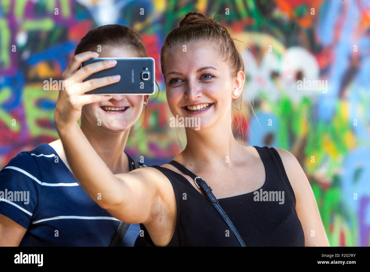 Due donne stanno facendo un selfie di fronte a John Lennon Wall Prague, Repubblica Ceca, ridendo al telefono cellulare Foto Stock