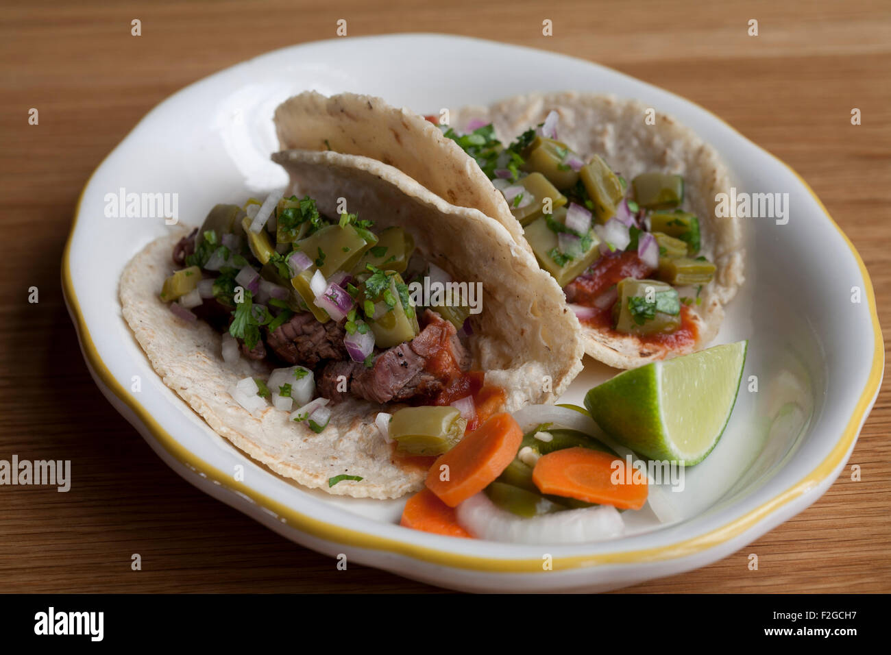Due carne asada tacos con nopales, chipotle e salsa su una piastra bianca sulla tavola di legno Foto Stock