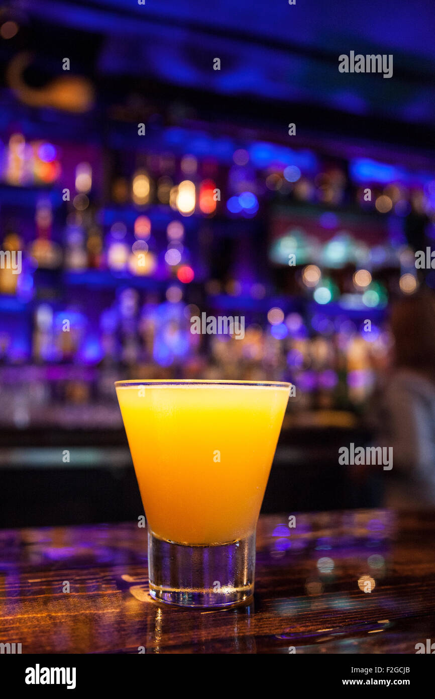 Colpo verticale di arancio brillante cocktail sul bar con viola al di fuori della messa a fuoco lo sfondo Foto Stock