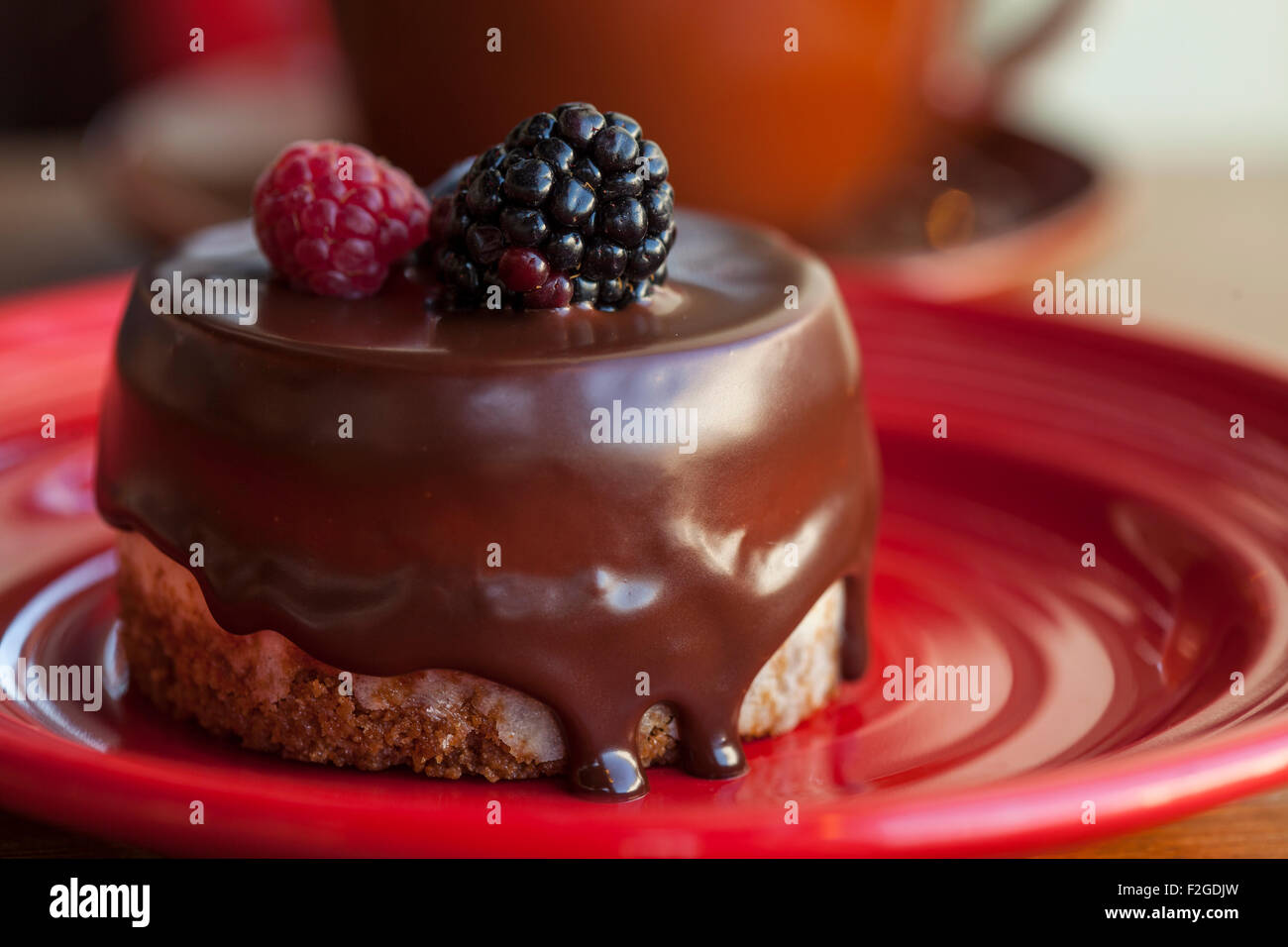 La panna acida cheesecake immersi nel cioccolato e guarnita con un lampone e un Blackberry Foto Stock