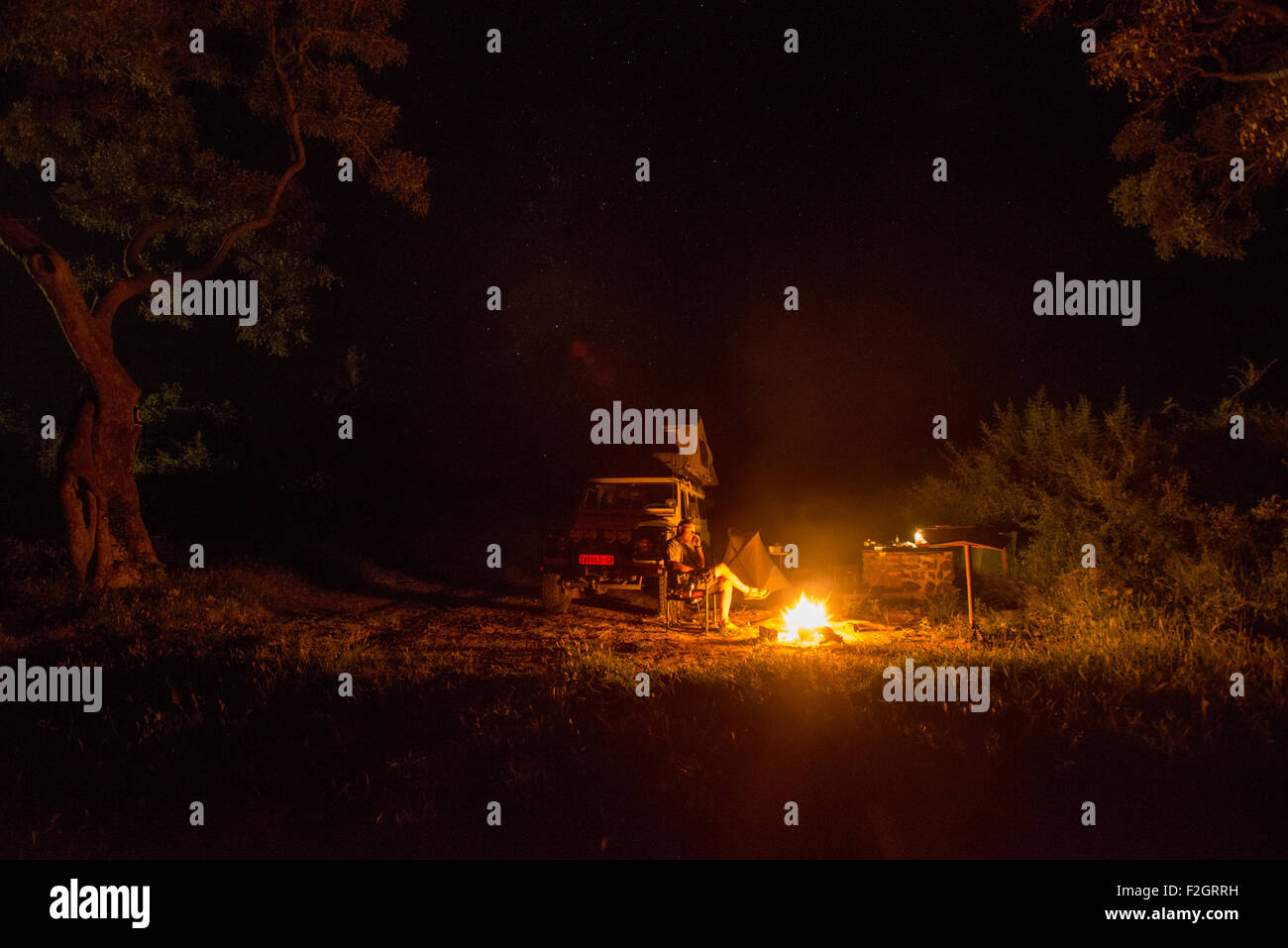 Uomo seduto in un incendio sul telefono con la sua Land Rover in background in Botswana, Africa Foto Stock