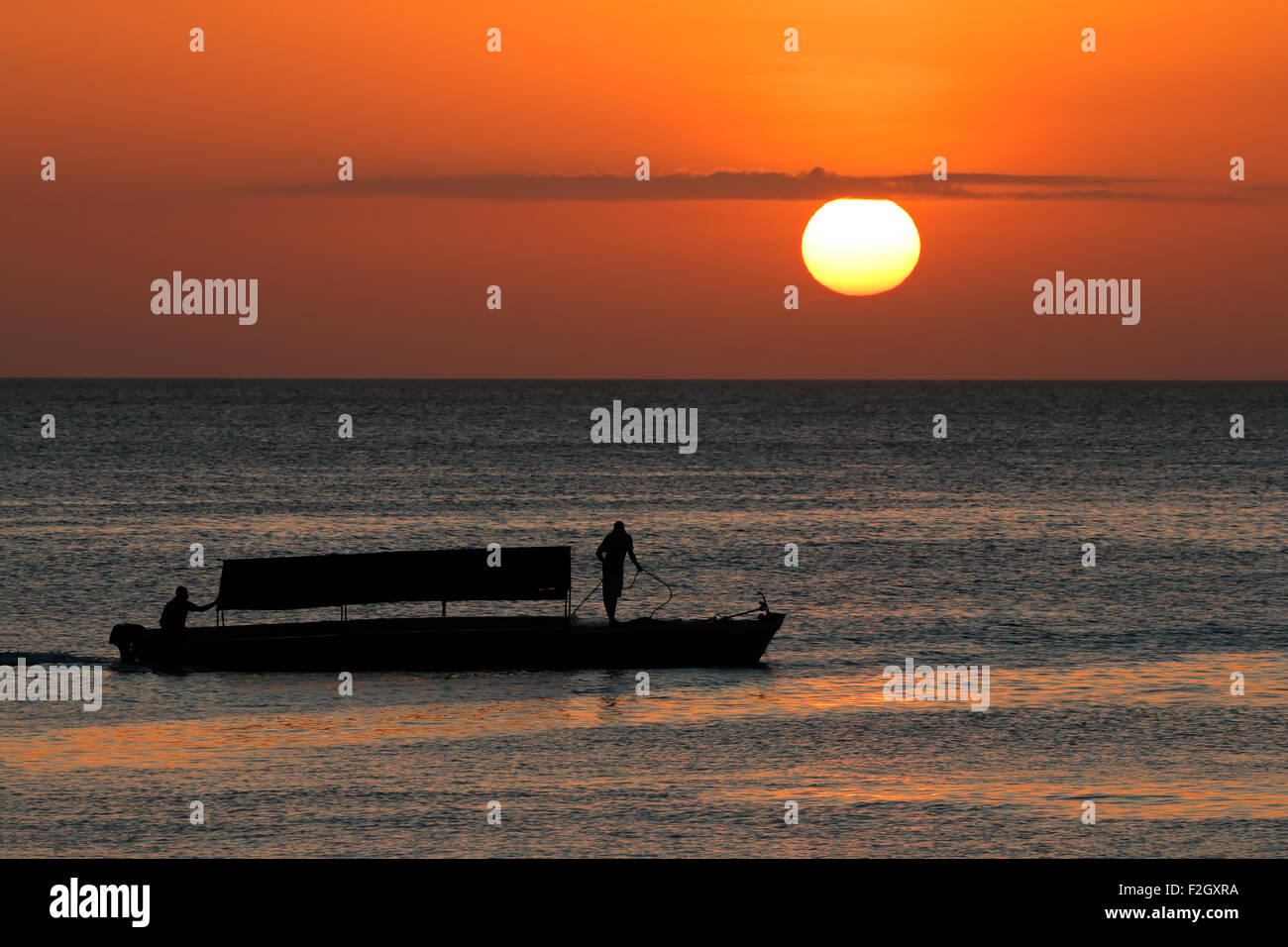 Silhouette di una barca contro un tramonto dorato, isola di Zanzibar Foto Stock