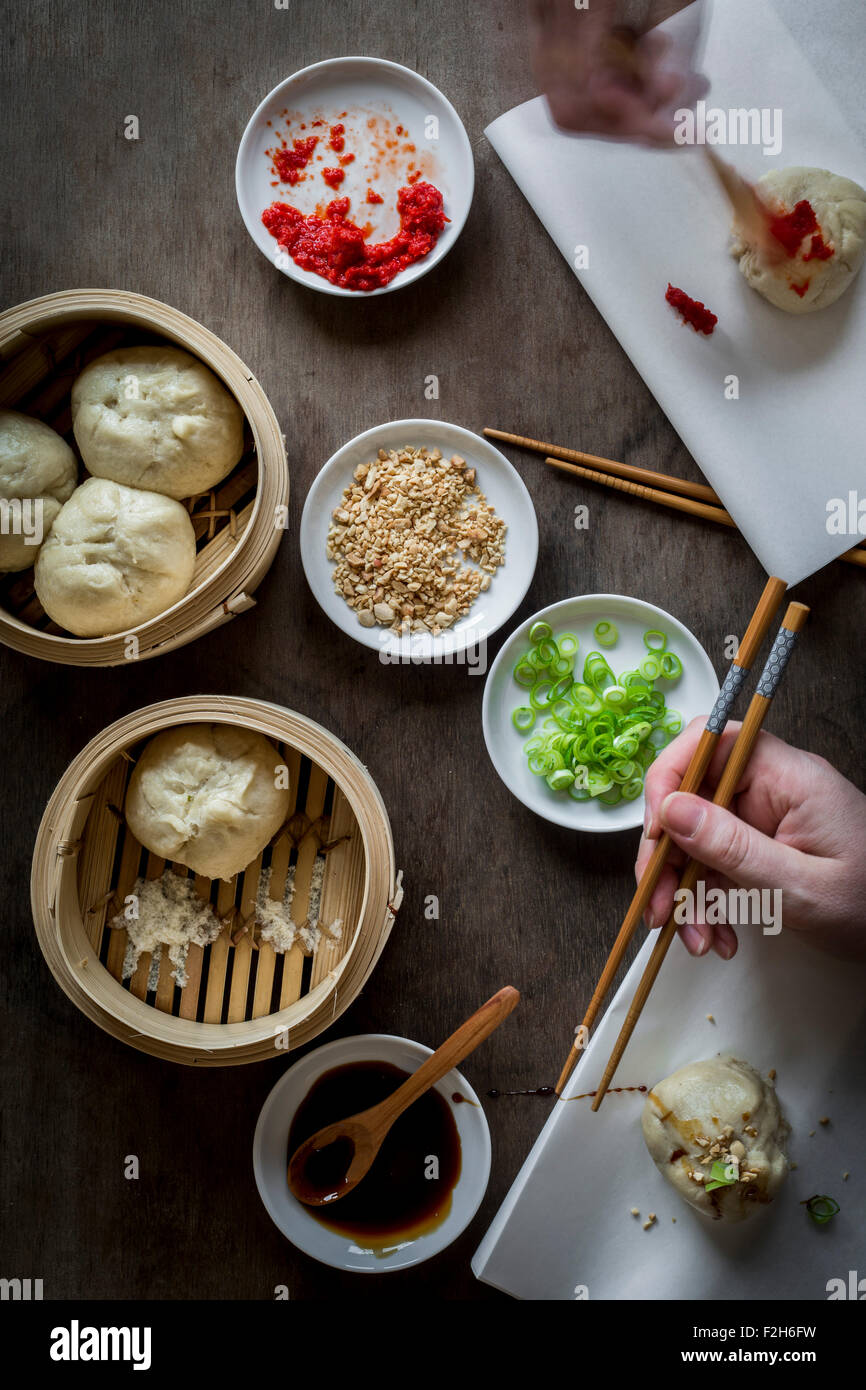 Due mani di mangiare Asian street food con bacchette di legno sul piano portapaziente con il piroscafo di bambù. Vista superiore Foto Stock
