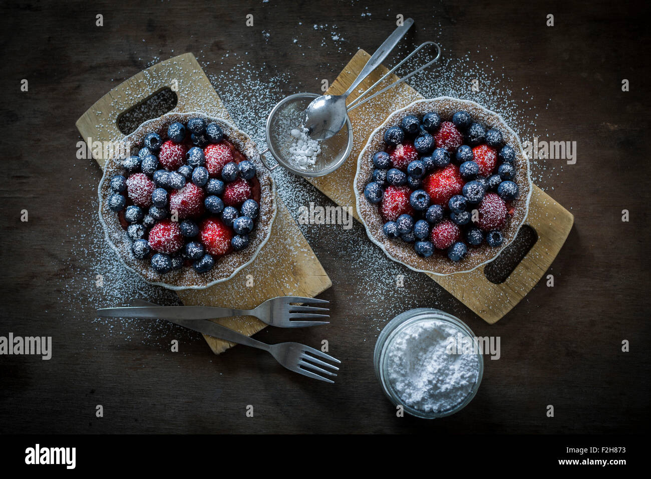 Berry tartetelets con zucchero a velo in piatti di cottura su piastre di legno con il buratto e torta forche. Vista superiore Foto Stock