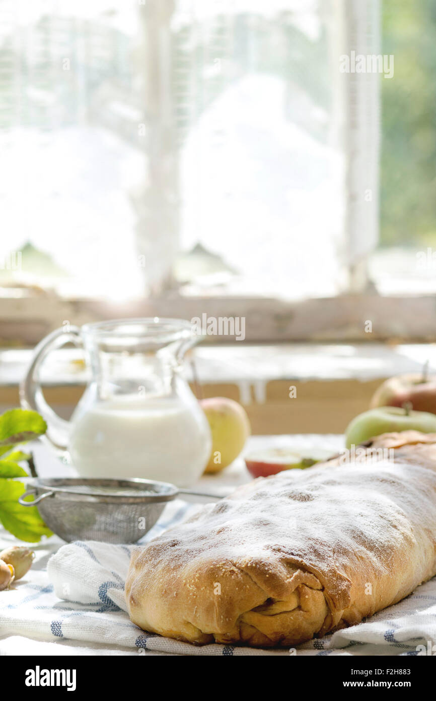 Freschi di forno in casa strudel di mele su asciugamano sul tavolo da cucina con la brocca del latte e le mele. Con finestra come sfondo. Rustico st Foto Stock