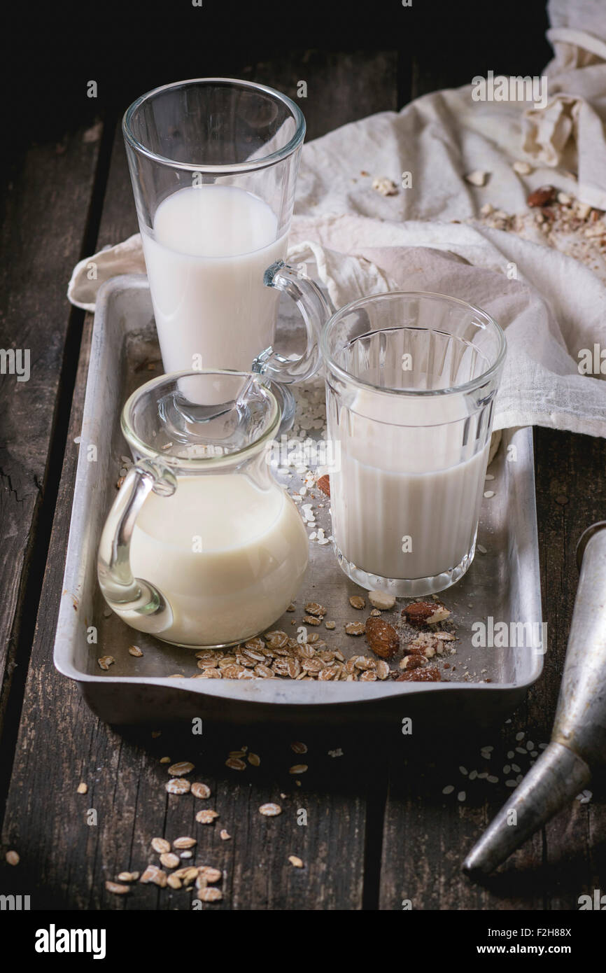 Set di non-latte (latte di riso, latte di mandorla e Latte di avena) in bicchieri di vetro e la brocca sulla vecchia vaschetta di alluminio con grani di riso, avena fla Foto Stock