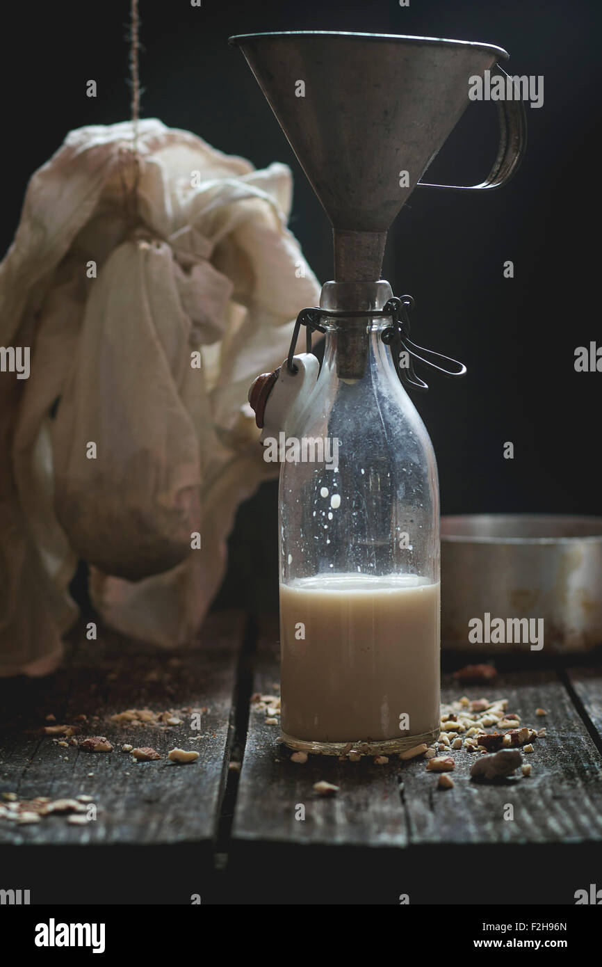 Retrò bottiglia di vetro di non-dairy latte di mandorla con il vecchio imbuto, massa di mandorle e vintage stoviglie in background. Rustico scuro st Foto Stock