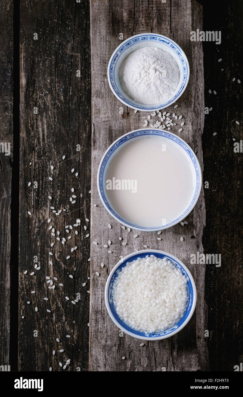 Stile cinese ciotole con latte di riso, farina di riso e riso imbevuto su un vecchio sfondo di legno con grani di riso di cui sopra. Vista dall'alto. Foto Stock