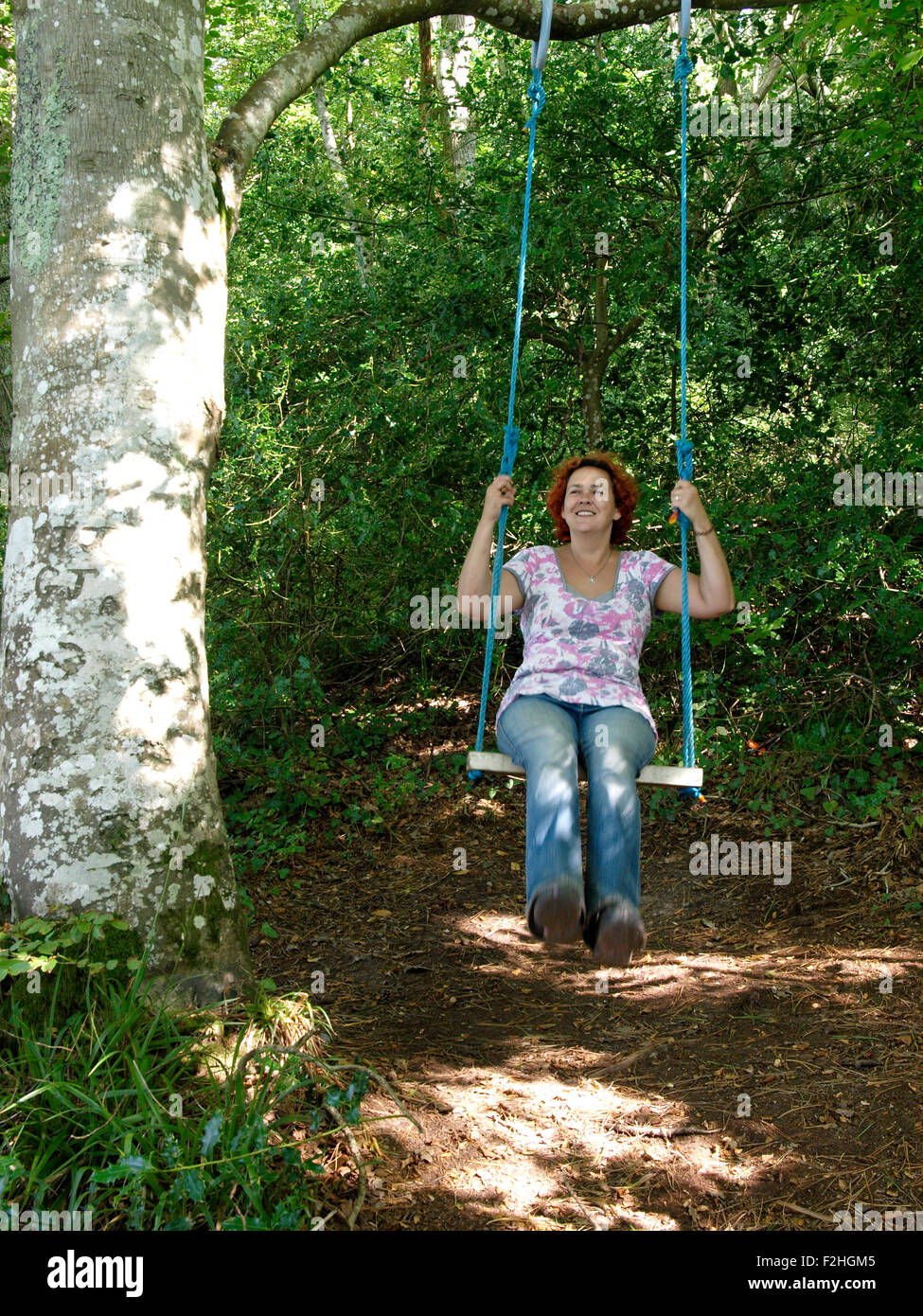 Quaranta anni di donna giocando su swing appeso a un albero, REGNO UNITO Foto Stock