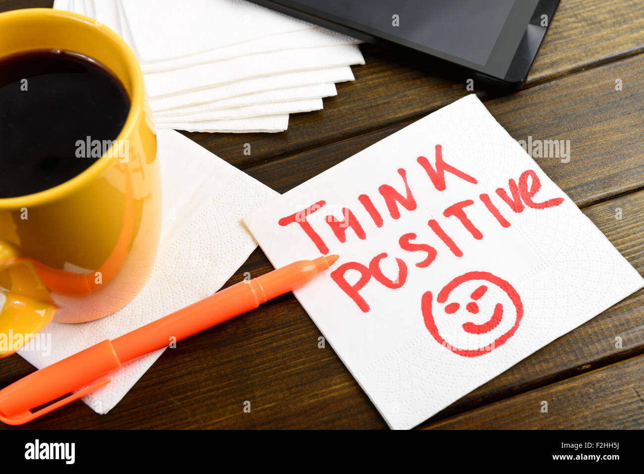 Pensare positivo la scrittura sul tovagliolo bianco intorno a penna di caffè e telefono sul tavolo di legno Foto Stock