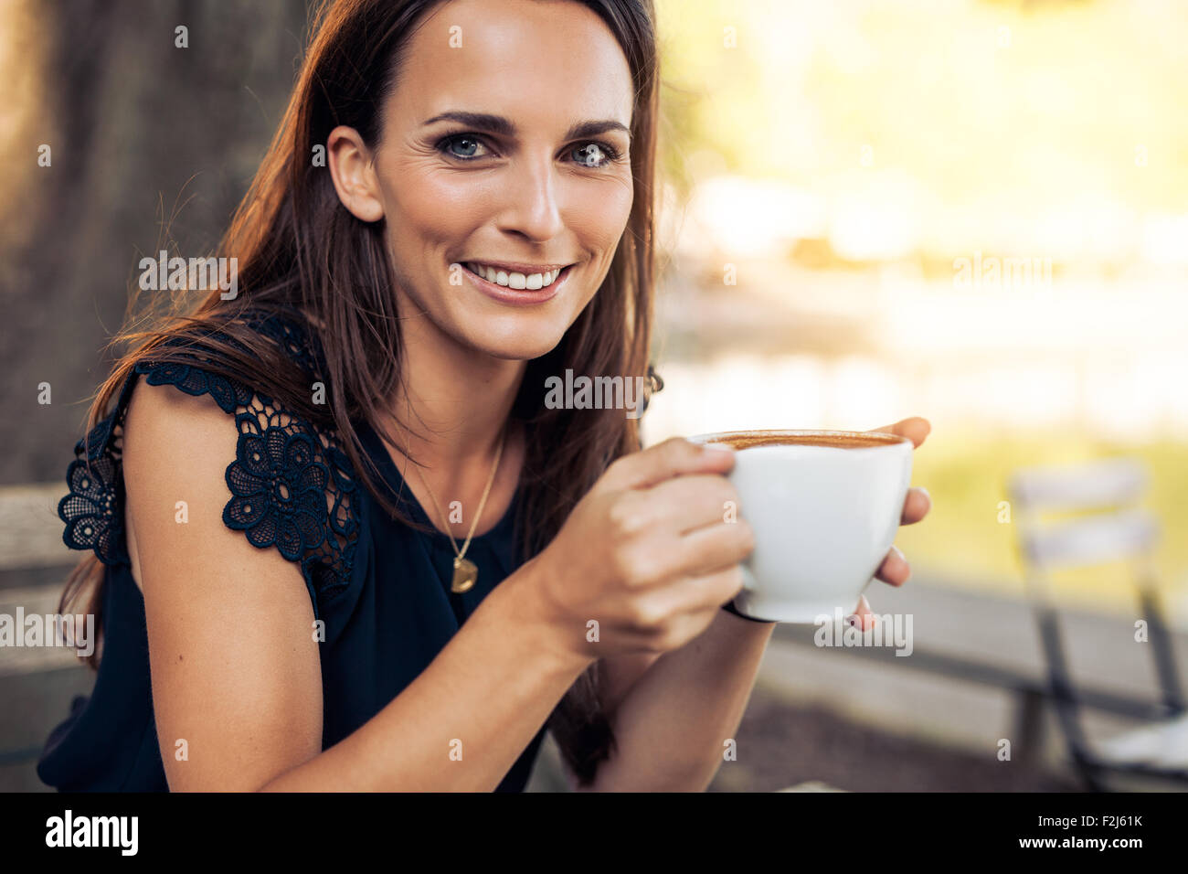 Ritratto di sorridente giovane donna con una tazza di caffè in mano guardando la fotocamera mentre presso il cafe. Foto Stock