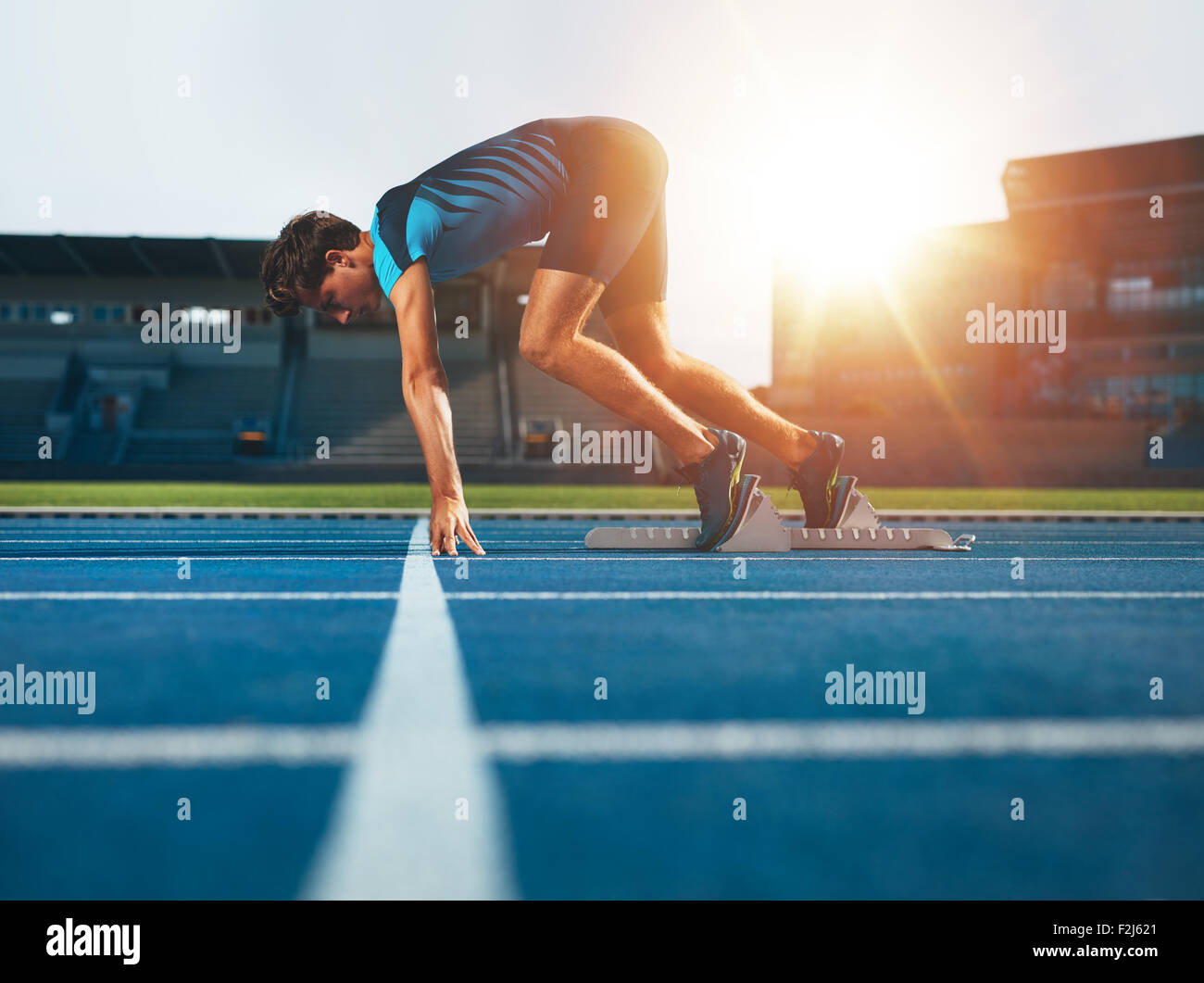 Atleta maschio sulla posizione di partenza in corrispondenza di atletica via di corsa. Runner mettere in pratica il suo avvio sprint in Athletics Stadium Racetrack. Foto Stock