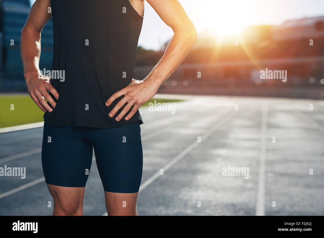 La sezione centrale colpo di atleta maschio permanente sulla pista con le mani sui fianchi su una intensa luce solare. Ritagliato colpo di giovane uomo r Foto Stock
