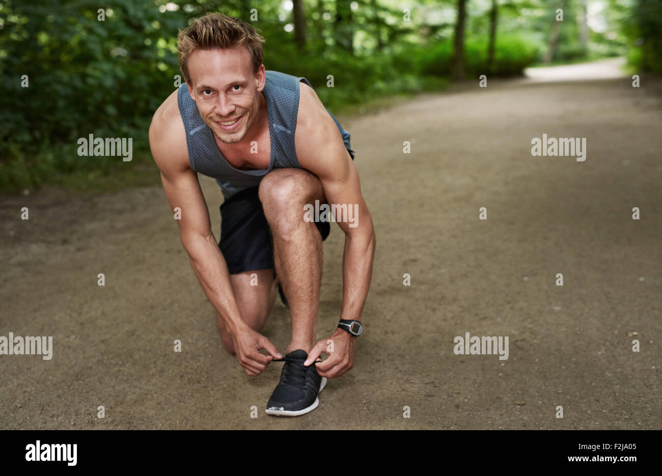 Muscolari sane uomo sorridente con la videocamera mentre fissa il suo stringa al parco. Foto Stock