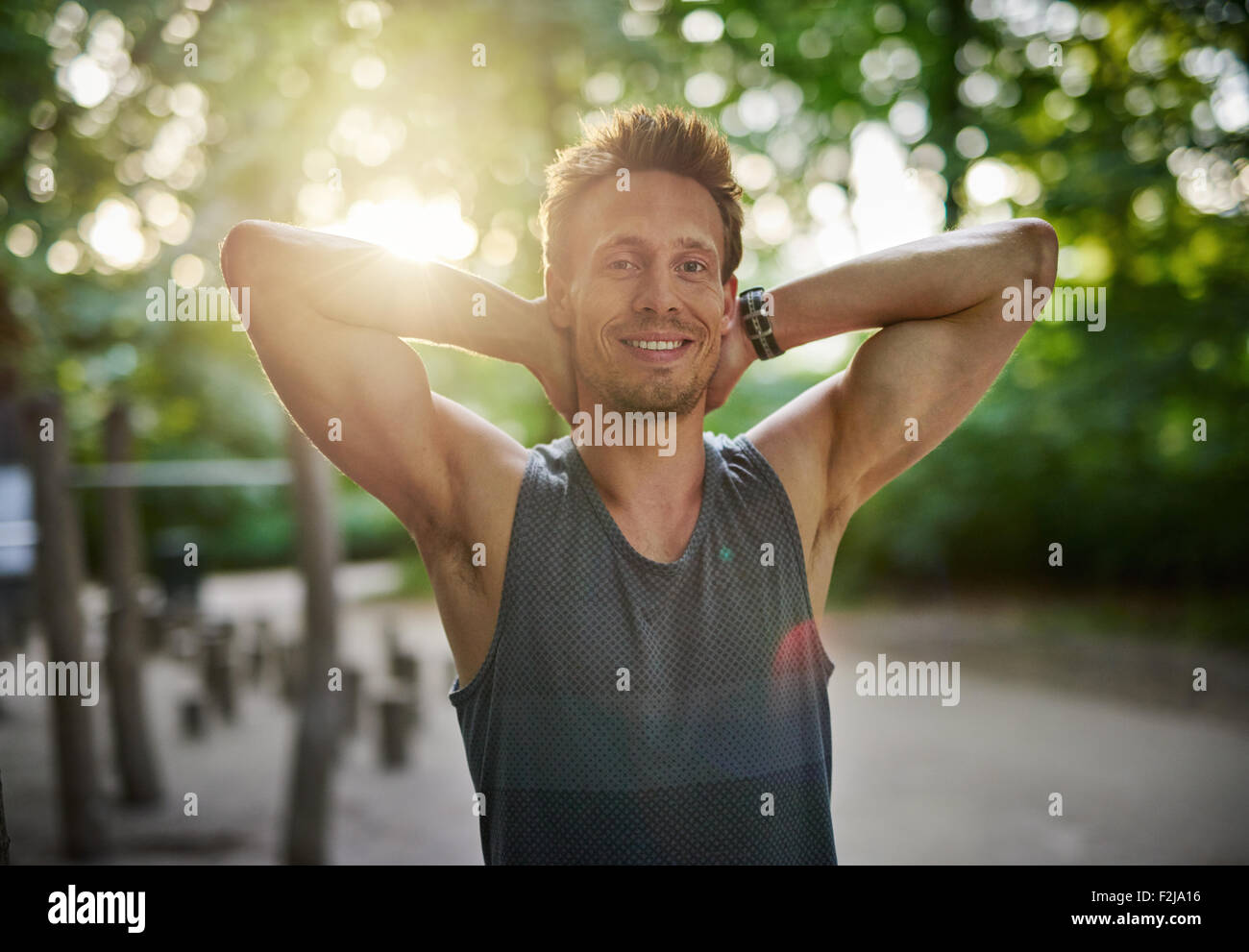 Mezzo Corpo colpo di una Preparazione Atletica Giovane Uomo presso il Parco di sorridere alla telecamera con le mani dietro la testa. Foto Stock