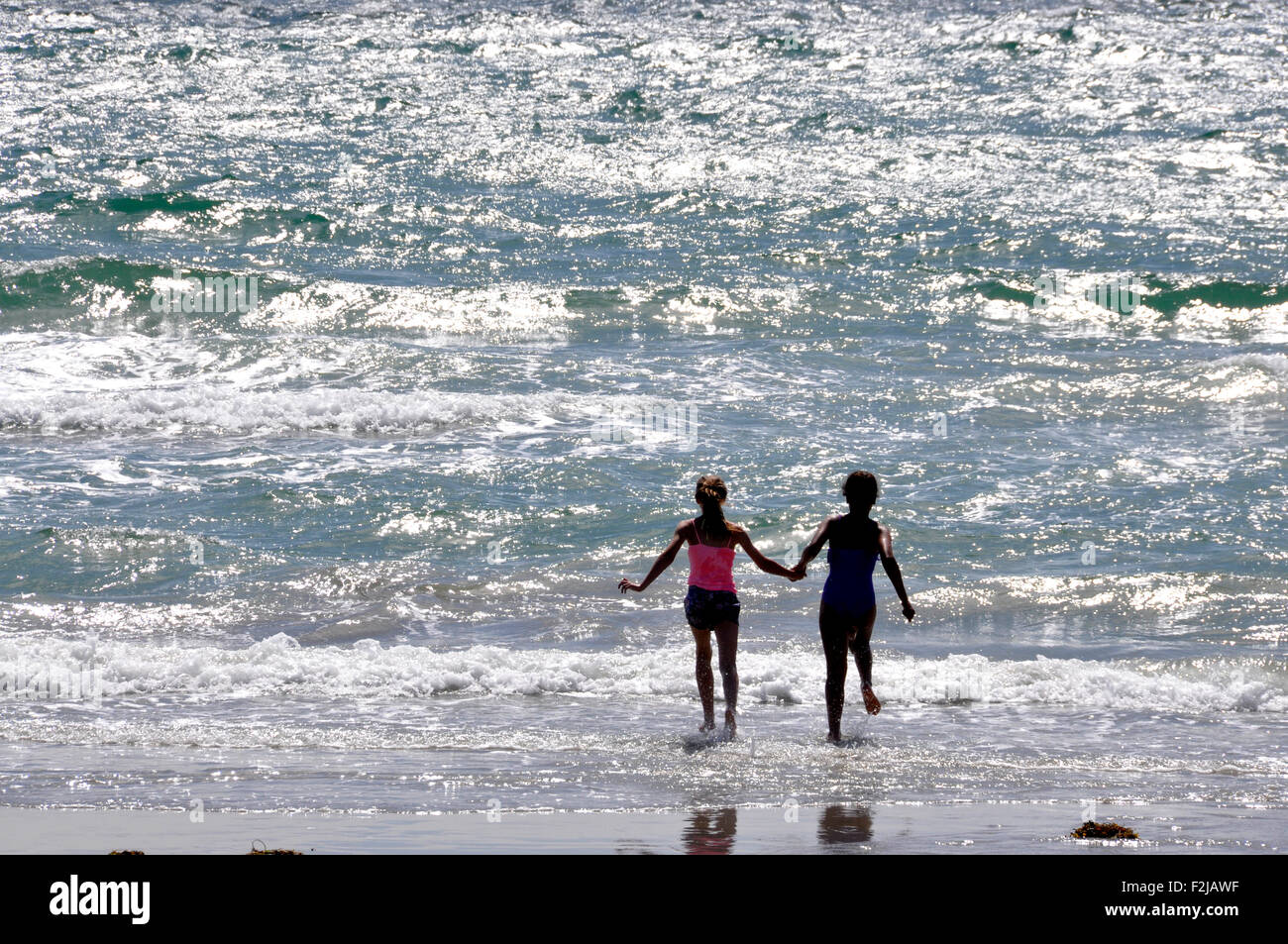 Contro la luce del sole seascape - spumanti onde che si infrangono sulla spiaggia di sabbia - coppia giovane esecuzione di mano in mano nel surf Foto Stock