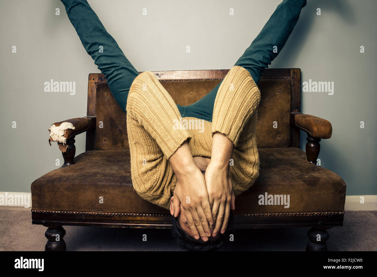 Giovane uomo disteso capovolto su un divano Foto Stock