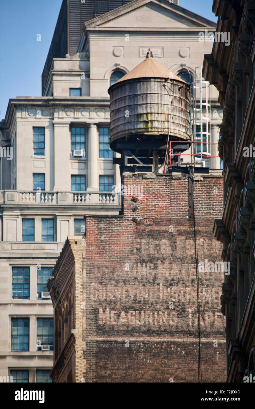 Un vecchio legno torre di acqua in cima a un edificio di mattoni con un nuovo e moderno edificio in background di Downtown Manhattan Foto Stock