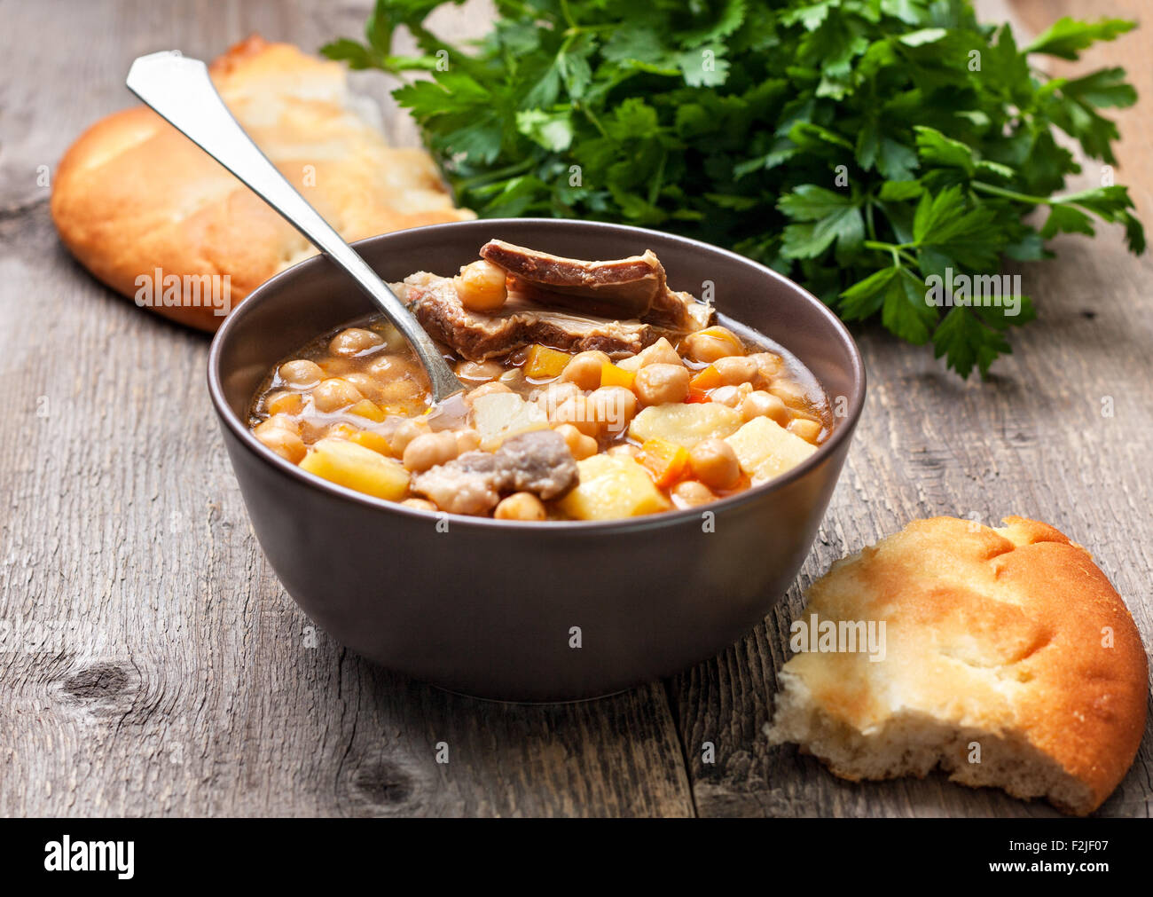 Minestra di ceci e agnello, pane piatto, prezzemolo su uno sfondo di legno Foto Stock